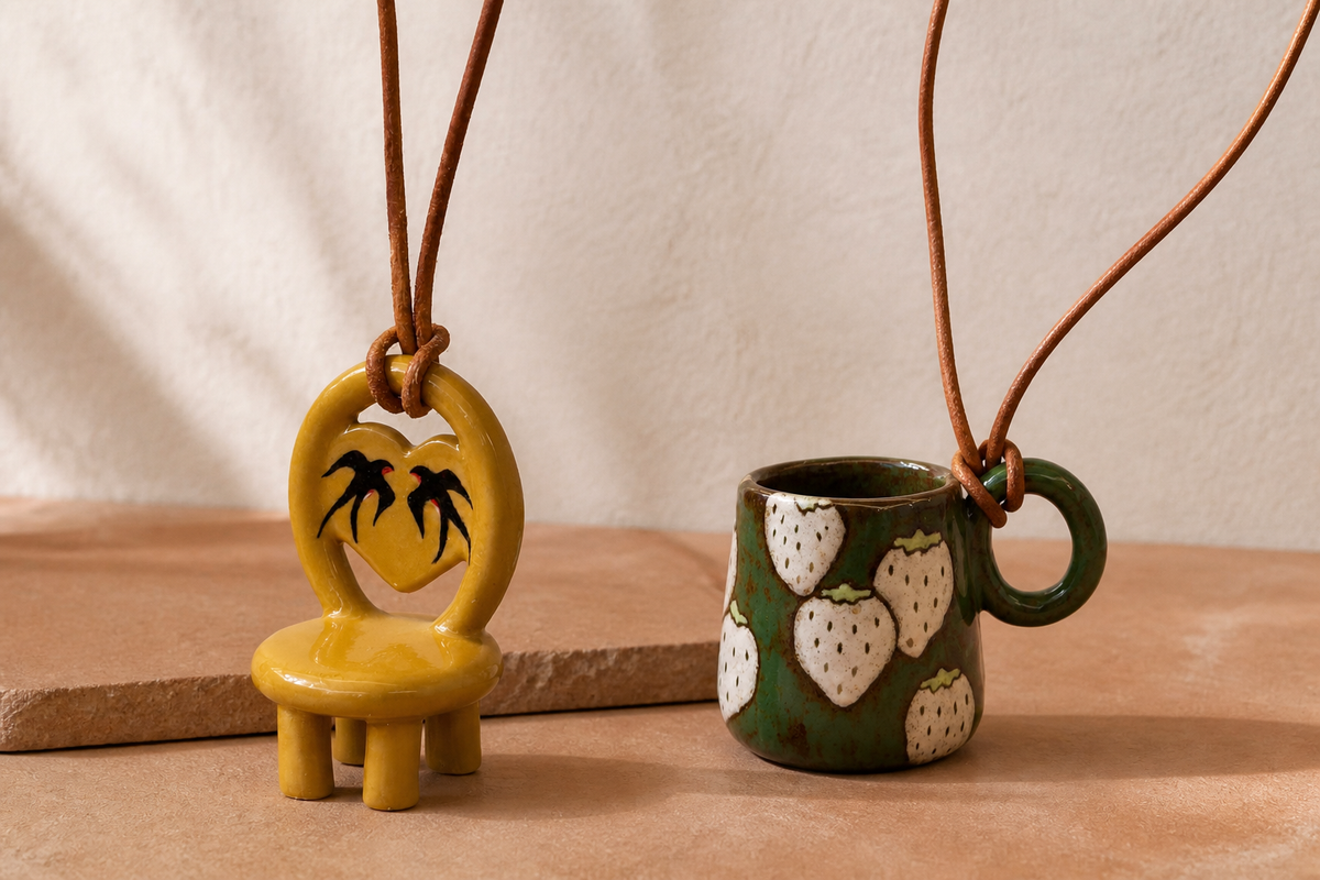 Swallow ceramic chair necklace and Strawberry ceramic cup necklace on a warm tabletop